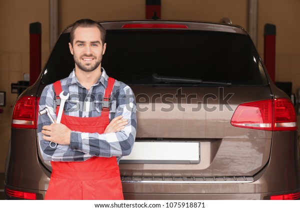Young\
auto mechanic with tools near car in service\
center