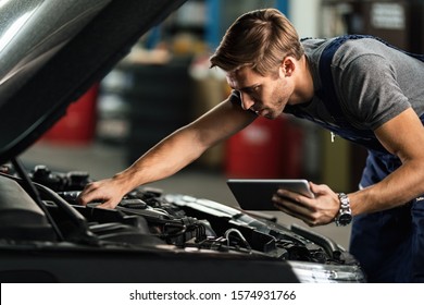 Young auto mechanic using digital tablet while repairing car engine in a workshop. 