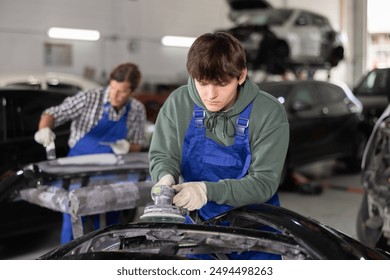 Young auto technician sanding car part using power sander with concentration, highlighting professional vehicle maintenance and repair skills in workshop - Powered by Shutterstock