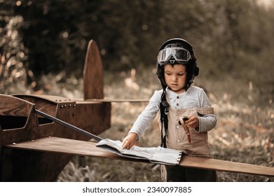 A young aviator boy near a homemade airplane in a natural landscape with a compass and a geographical map. The authentic mood of the picture. Cartography. Vintage.