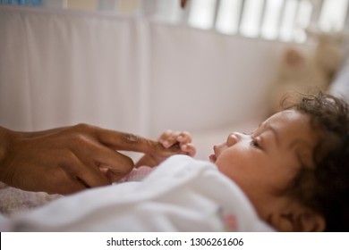 Young Baby Holding Onto Her Parent's Finger While Lying In Her Cot.