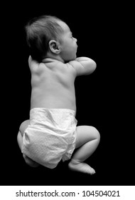 A Young Baby Is Laying Down On Their Tummy On A Black Isolated Background. The Babies Back And Diaper Is Showing. Use It For A Growth Or Dream Concept.