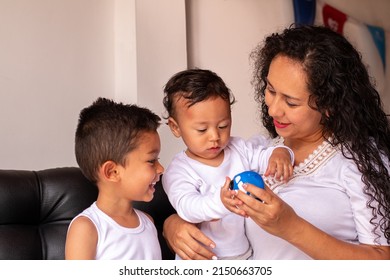 A young baby and toddler playing with their mother with a toy cart. Frizzy haired latin mother teaching her children to play.