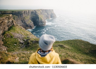 Young backpacker girl standing on the  Cliffs of Moher in yellow jacket and cap - Powered by Shutterstock