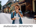 Young backpacker looking for direction on a map while walking through the town.