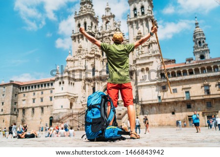 Young backpacker man pilgrim standing with raised arms on the Obradeiro square (plaza) - the main square in Santiago de Compostela as a end of his Camino de Santiago pilgrimage.