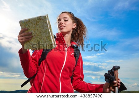 Young backpacker standing on a green meadow at sunny day and looking into a map