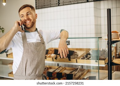 Young baker standing by the counter and talking on the phone - Shutterstock ID 2157258231