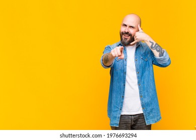 Young Bald And Bearded Man Smiling Cheerfully And Pointing To Camera While Making A Call You Later Gesture, Talking On Phone