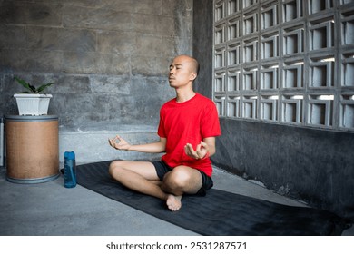 A young bald Indonesian man is stretching while doing yoga at home, the concept of a healthy lifestyle through exercise. - Powered by Shutterstock