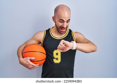 Young bald man with beard wearing basketball uniform holding ball looking at the watch time worried, afraid of getting late  - Powered by Shutterstock