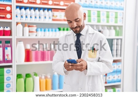 Young bald man pharmacist using smartphone working at pharmacy