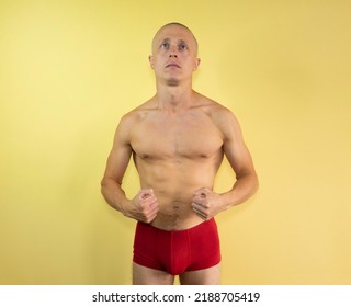 Young Bald Man In Red Shorts Looks Up On A Yellow Isolated Background. Man Portrait. Naked Man. Muscle Man