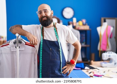 Young Bald Man Tailor Smiling Confident Leaning On Clothes Rack At Clothing Factory