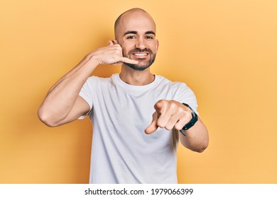 Young Bald Man Wearing Casual White T Shirt Smiling Doing Talking On The Telephone Gesture And Pointing To You. Call Me. 