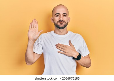 Young Bald Man Wearing Casual White T Shirt Swearing With Hand On Chest And Open Palm, Making A Loyalty Promise Oath 