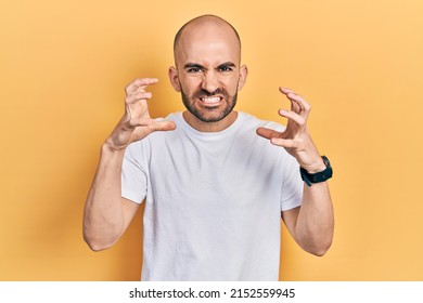 Young bald man wearing casual white t shirt shouting frustrated with rage, hands trying to strangle, yelling mad 
