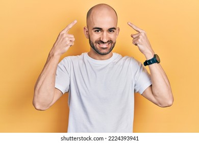 Young bald man wearing casual white t shirt smiling pointing to head with both hands finger, great idea or thought, good memory  - Powered by Shutterstock