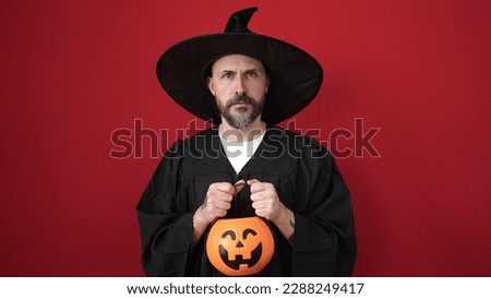 Young bald man wearing wizard costume holding pumpkin halloween basket over isolated red background
