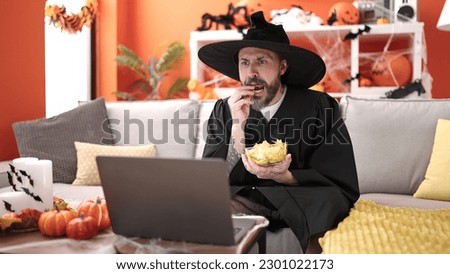 Young bald man wearing wizard costume eating chips potatoes watching movie at home