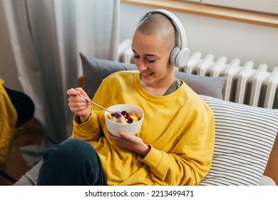 Young Bald Woman With Headphones Eats Fruit Salad In Her Room