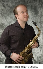 Young Balding Man Posing In Front Of Portrait Backdrop With Saxaphone