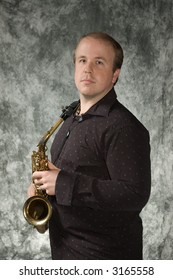 Young Balding Man Posing In Front Of Portrait Backdrop With Saxaphone