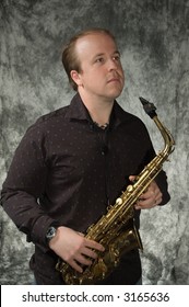 Young Balding Man Posing In Front Of Portrait Backdrop With Saxaphone