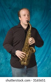 Young Balding Man Posing In Front Of Portrait Backdrop With Saxaphone