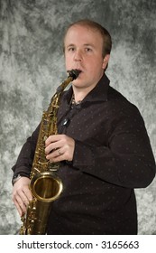 Young Balding Man Posing In Front Of Portrait Backdrop With Saxaphone