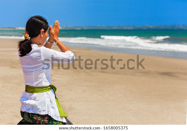 Young balinese women praying with namaste hands\
on sea beach at ceremony before silence day Nyepi. Religious\
holidays, traditional festivals, rituals, art, culture of\
Indonesian people on Bali\
island.