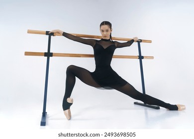 a young ballerina in black leotard shows an eversion of the feet and stretching while warming up at the barre - Powered by Shutterstock