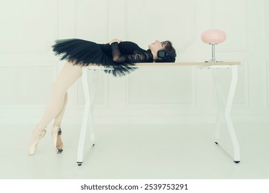 a young ballerina in a black tutu sitting on a table listening to music with headphones, business style, total black - Powered by Shutterstock