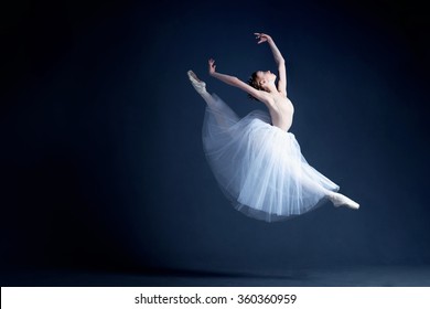 Young ballerina with a perfect body is dancing in the photo studio. The dancer wears a fashionable dress. The photo is taken in minimal style, showing the beauty of a such classical art like ballet. 