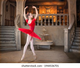 A young ballerina in a red tutu is dancing against the background of the theatrical scenery of the palace.