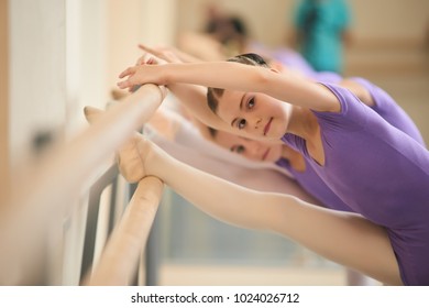 Young Ballerina Stretching Before Ballet Practice. Ballet Girl Training Her Flexibility At Ballet Barre In Hall. Safely Technique For Stretching.