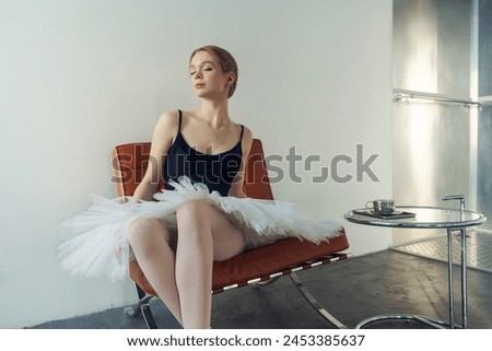 a young ballerina in a tutu and pointe shoes is sitting on an armchair next to a table with a cup of coffee