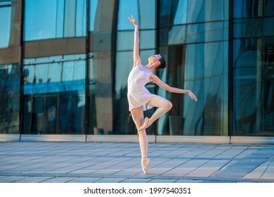young ballerina in a white leotard dancing on pointe shoes against the backdrop of a cityscape