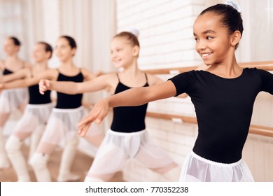 Junge Ballerinas, die in der Ballettklasse proben. Sie führen verschiedene choreographische Übungen durch. Sie stehen in verschiedenen Positionen in der Nähe der Ballettbühne.