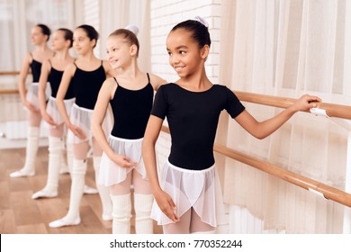 Young ballerinas rehearsing in the ballet class. They perform different choreographic exercises. They stand in different positions near the ballet barr.