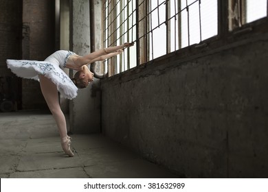 Young ballet dancer posing next to windows in an old industrial building. She is standing on pointes while she holds the grille during tilting back. Indoor. Horizontal. - Powered by Shutterstock