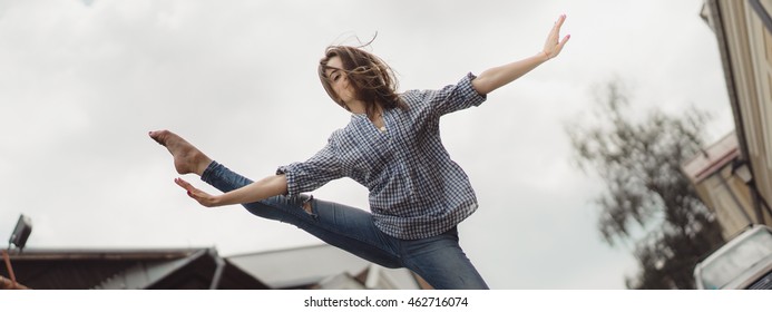 Young ballet dancer posing on a pedestrian street . Beautiful girl showing ballet movements on the pavement .