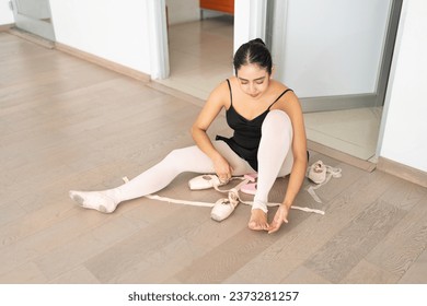 young ballet dancer preparing before class; hispanic ballerina getting ready putting on pointe shoes - Powered by Shutterstock - Get 15% off with code: PIKWIZARD15