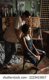 Young Barefoot Artist Standing Near Sexy African American Woman In Denim Overalls Sitting In Workshop