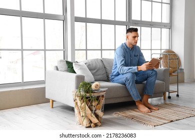 Young barefoot man reading book on sofa at home