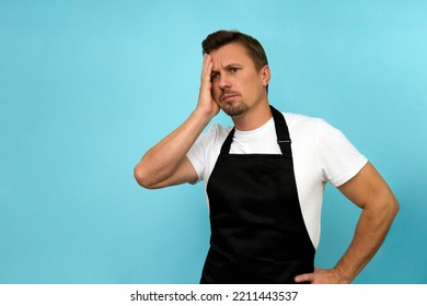 Young Barista In Black Apron And White T-shirt On Blue Background With Copy Space. Man Wearing Chef Apron, Close-up