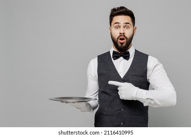 Young Barista Male Waiter Butler Man Wear White Shirt Vest Elegant Uniform Work At Cafe Hold Carrying Point Finger On Metal Tray Isolated On Plain Grey Background Studio. Restaurant Employee Concept