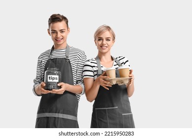 Young Baristas With Tip Jar And Cups Of Coffee On Light Background