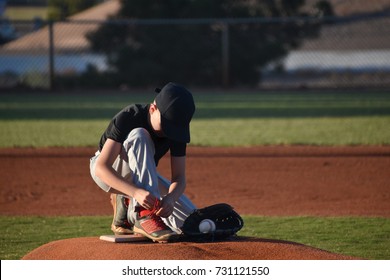 Young baseball playing stopping to tie shoe laces on pitcher's mound - Powered by Shutterstock