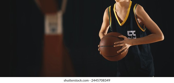 Young basketball player with classic ball. Basket in background. Junior level basketball player holding game ball. Basketball training session for kids - Powered by Shutterstock